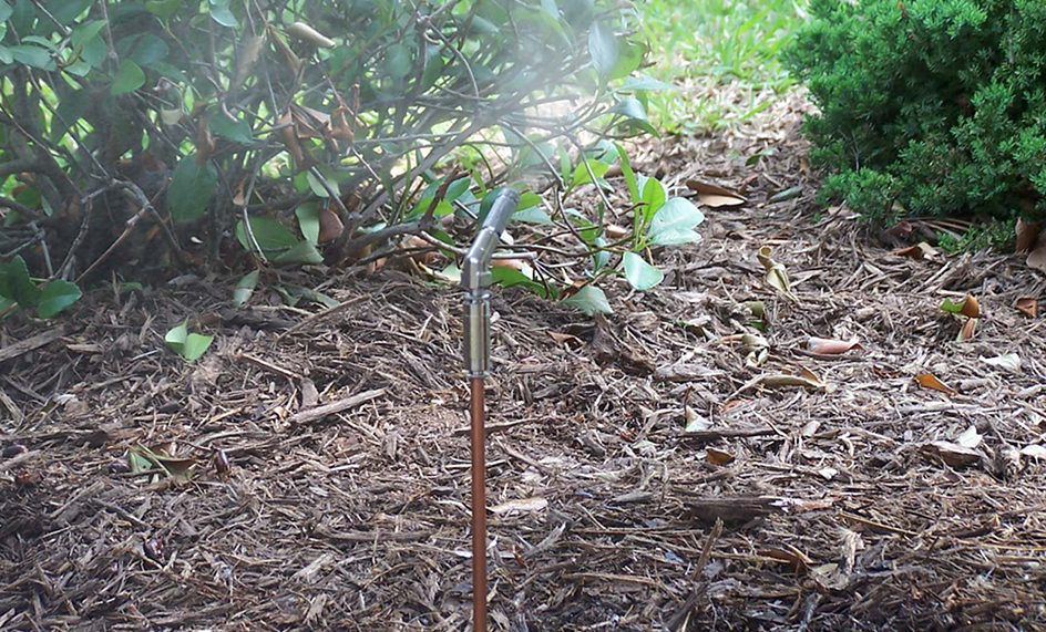 A mosquito misting nozzle rising from the bushes to spray mosquito mist